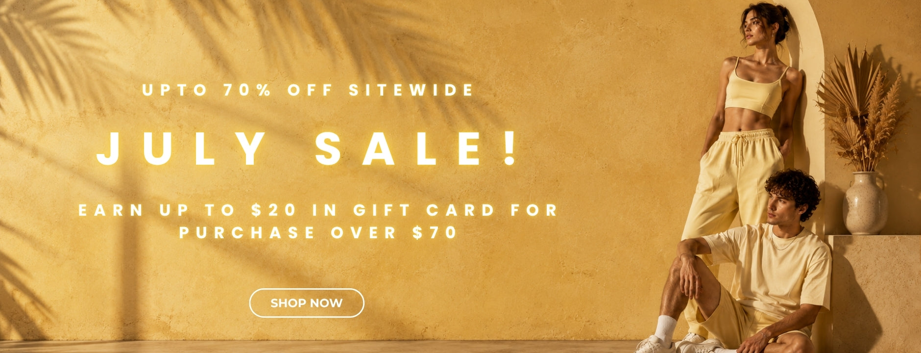 A promotional banner for a July sale featuring a woman in a beige crop top and shorts and a man in a beige t-shirt and shorts, posed against a warm yellow textured wall with palm shadows and a potted plant. Large text reads 'JULY SALE!' with additional discount and gift card offer text.